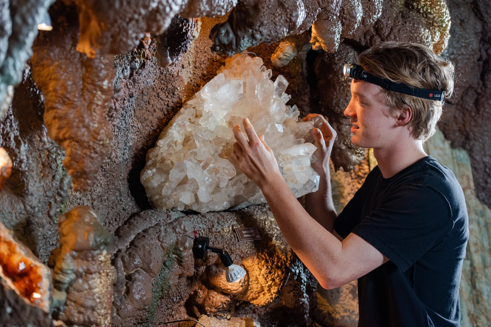 A visitor with a headlamp touching a large quartz crystal cluster on the cave wall at Crystal Caves