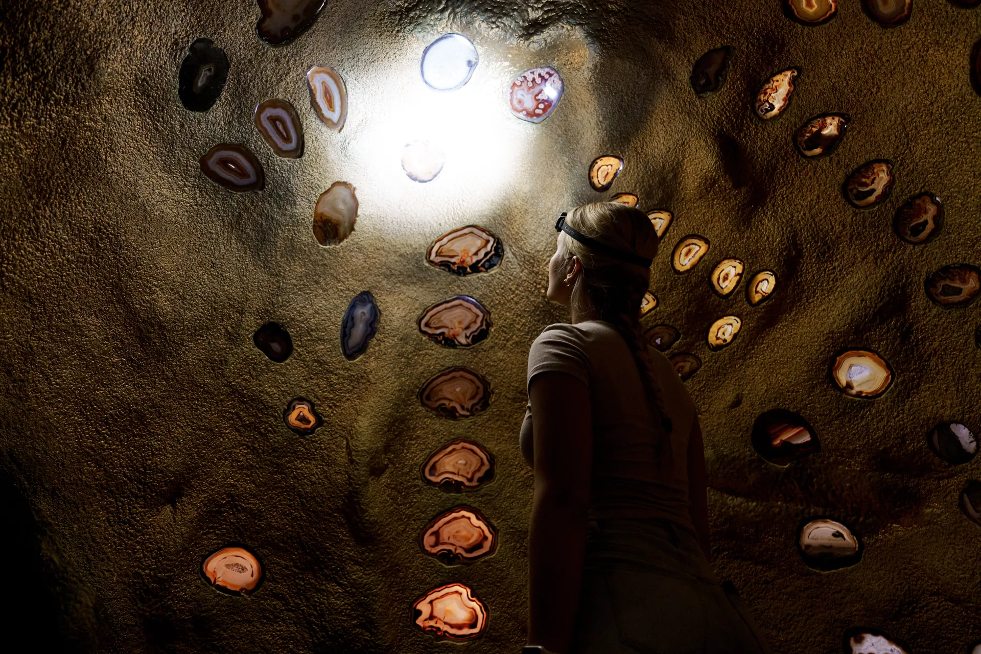 A visitor explores the agate dome inside Crystal Caves, lit by her headlamp