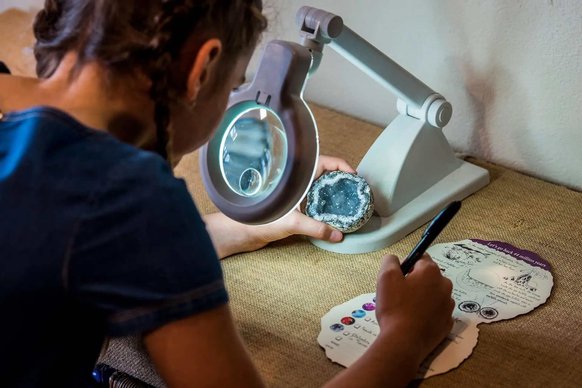 Young visitor examining a geode under a magnifier and writing on a worksheet